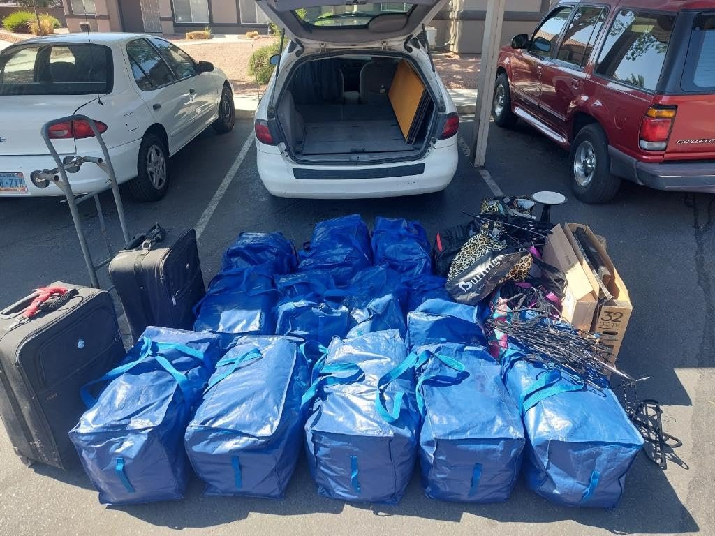 Open car trunk with blue bags and assorted items on the ground