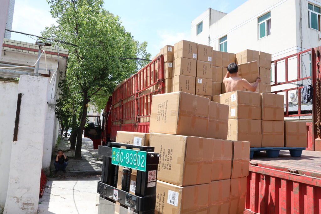 Workers loading packed boxes of tote bags onto red freight truck for delivery