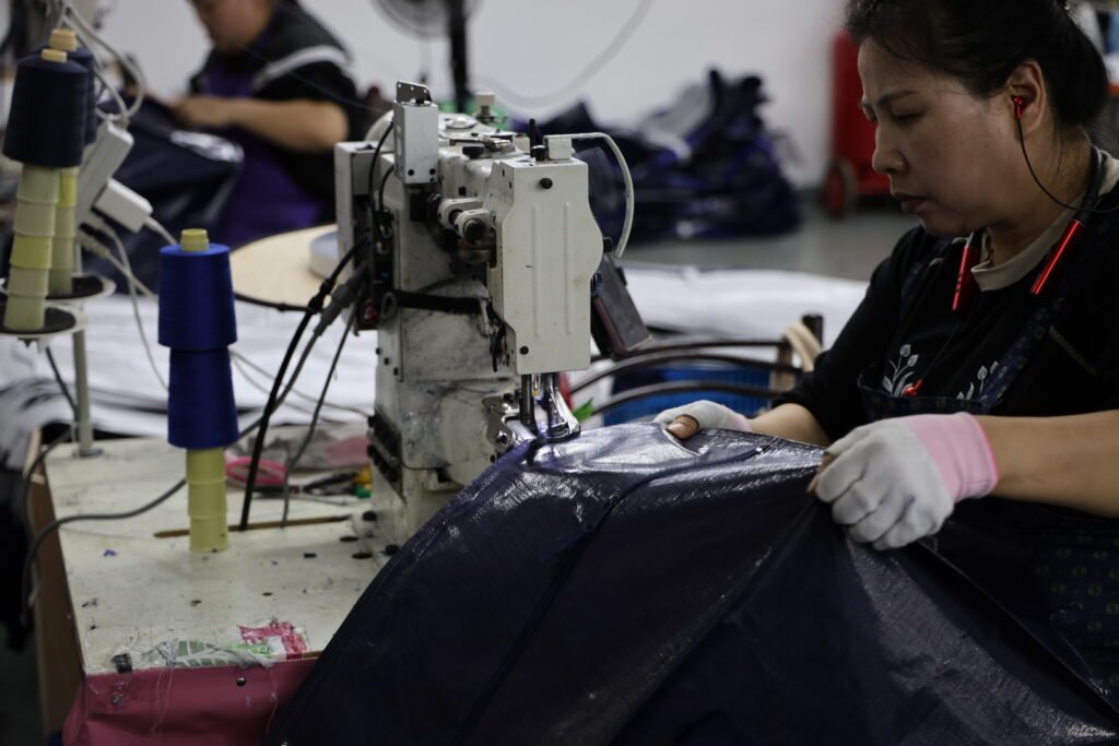 Worker sewing heavy-duty storage bag on industrial sewing machine in factory setting