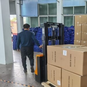Worker moving stacked cardboard boxes on pallet with forklift in canvas bag factory warehouse for bulk shipping