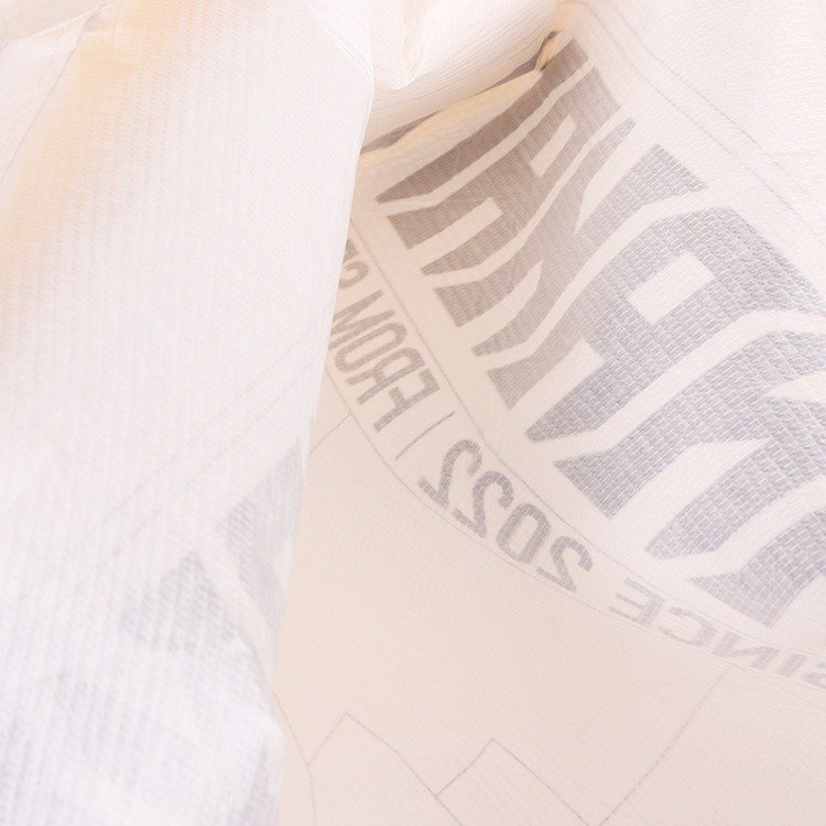 Close-up view of white non-woven fabric tote bag material with printed gray text, ideal for custom logo shopping bags and eco-friendly packaging.