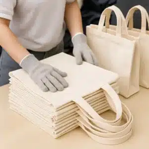 White reusable cotton tote bags stacked and prepared for packaging in production area.