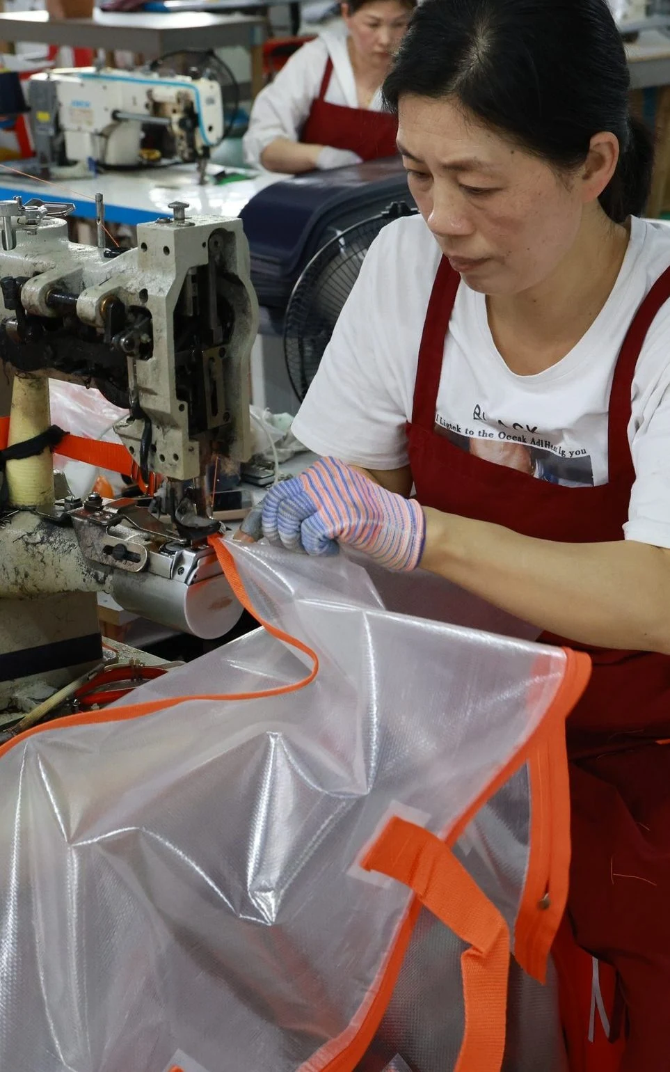 Moving Bags Manufacturing Tiiocti Worker Sewing Orange Edge Binding Onto A Transparent Moving Bag At An Industrial Sewing Machine