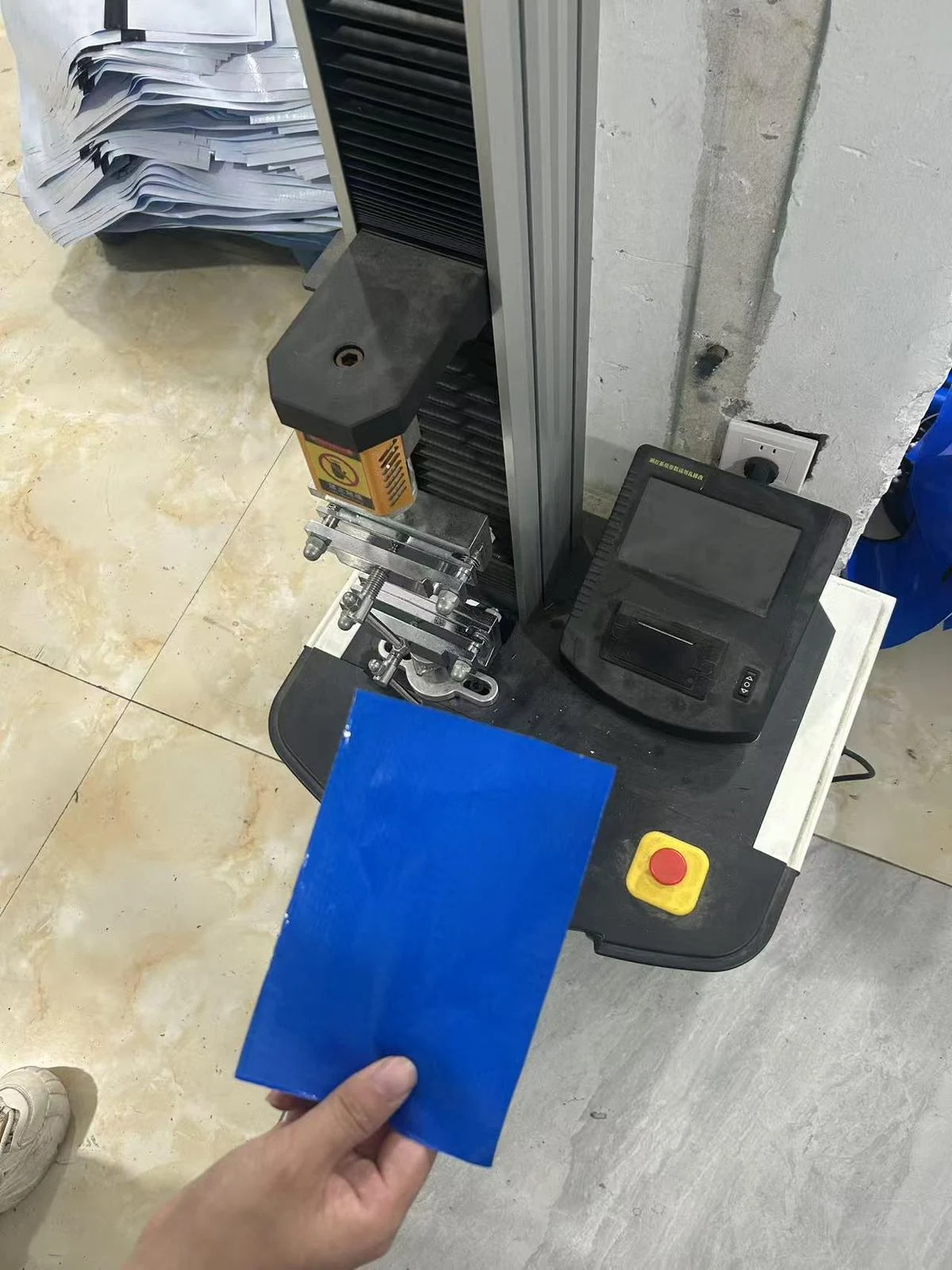 Moving Bags Manufacturing Tiiocti Blue Bag Material Sheet Held In Front Of The Tensile Tester For Sample Preparation