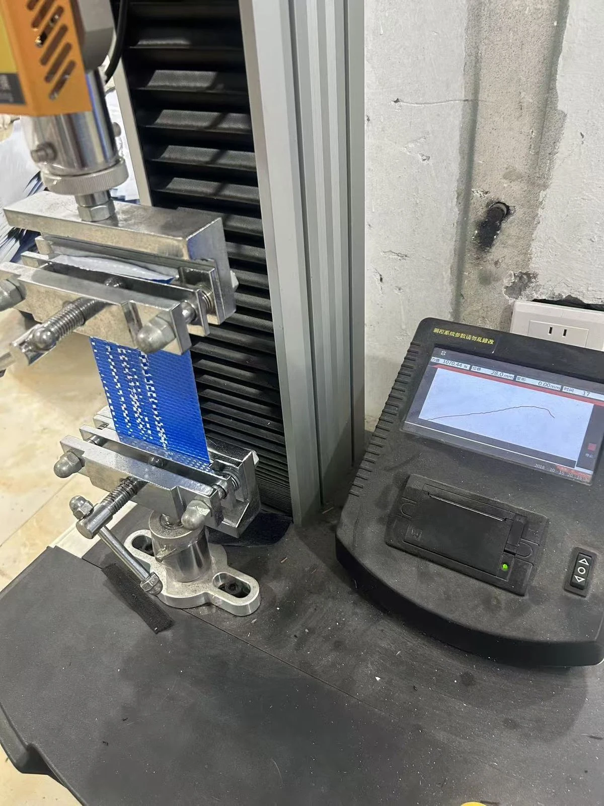 Moving Bags Manufacturing Tiiocti Blue Woven Bag Material Strip Between Tensile Test Clamps Beside The Measurement Display