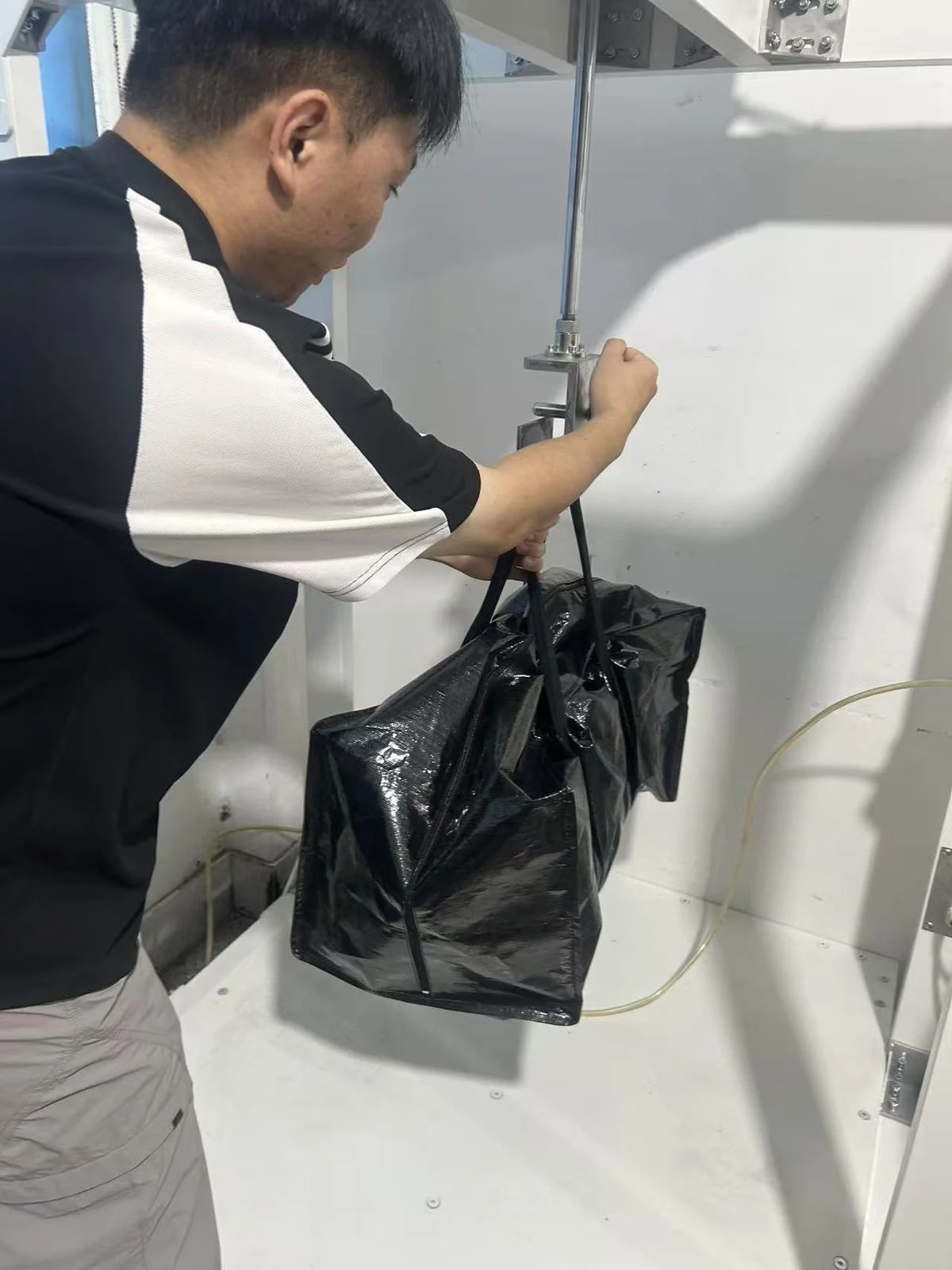 Moving Bags Manufacturing Tiiocti Technician Attaching The Handles Of A Filled Black Moving Bag To The Oscillation Test Fixture
