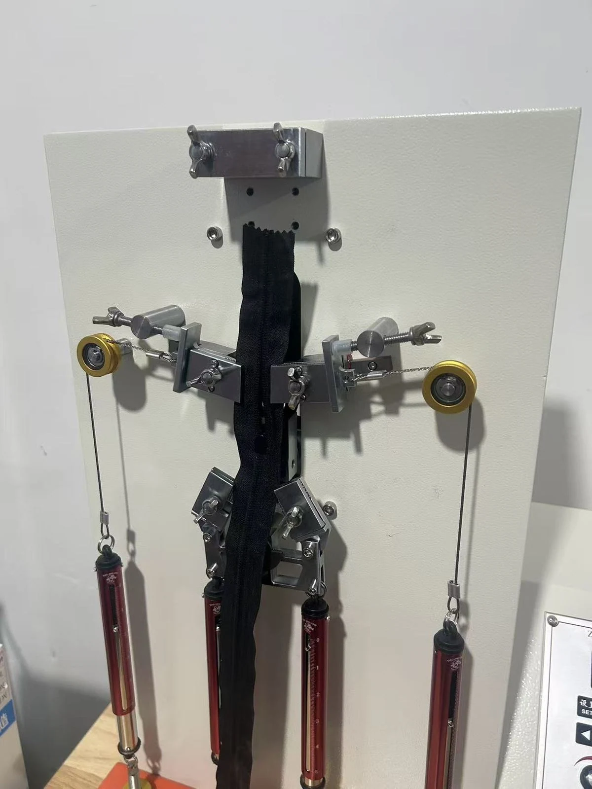 Moving Bags Manufacturing Tiiocti Black Zipper Sample Mounted Vertically In Test Clamps With Hanging Weights On The Machine