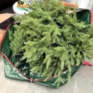 Open green storage bag filled with disassembled artificial Christmas tree branches