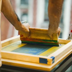 Hands screen printing with colorful ink using wooden squeegee Manual screen printing process on fabric, ideal for custom logo printing on tote bags and other textile products