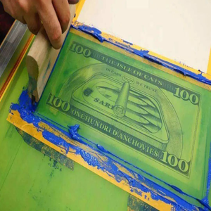 Screen printing blue ink on humorous money design Close-up of screen printing process applying green money bill design on fabric, ideal for custom logo and pattern printing on tote bags