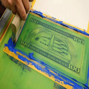 Close-up of screen printing process applying green money bill design on fabric, ideal for custom logo and pattern printing on tote bags