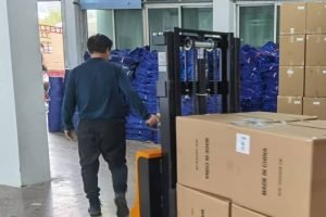 Worker moving stacked cardboard boxes on pallet with forklift in canvas bag factory warehouse for bulk shipping