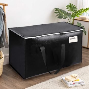 Black heavy-duty moving bag with zipper and handles, placed in a bedroom for clothes or blanket storage