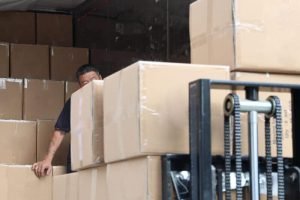 Workers loading packed boxes of custom canvas tote bags into a shipping container for international delivery